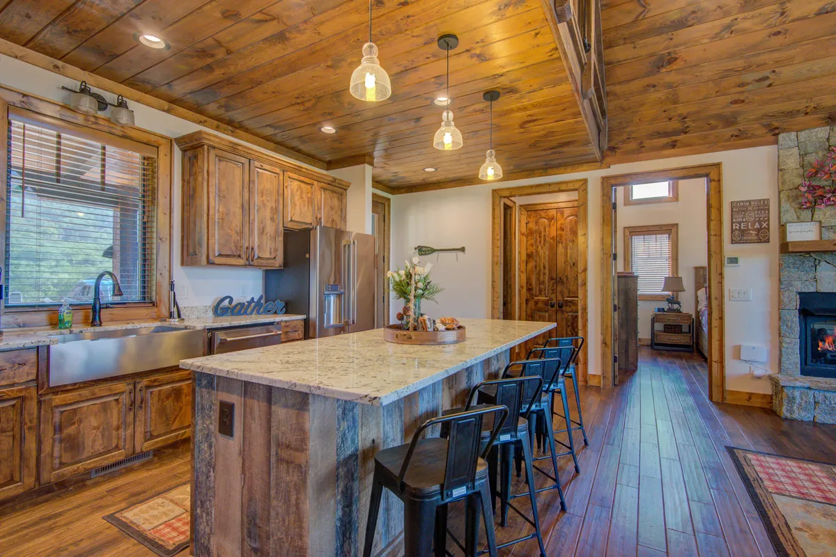 A welcoming kitchen scene featuring a large island with seating, gleaming stainless steel appliances, wooden cabinetry, ample natural light streaming through the windows, and decorative accents such as fresh flowers.