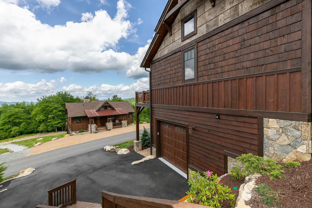 A welcoming view of the main house with a wooden facade and stone accents, surrounded by lush greenery. The setting is serene, yet hints at social gatherings and outdoor activities with family and friends, with nature trails nearby.
