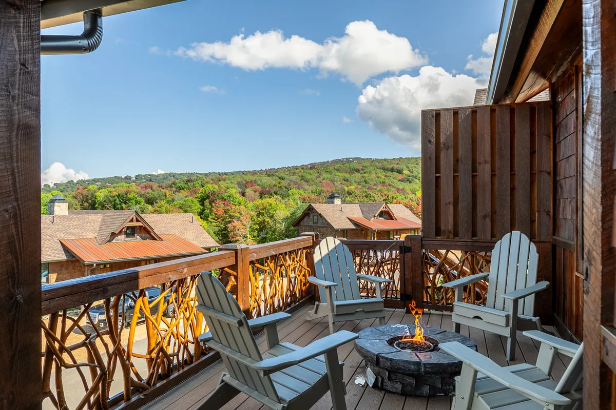 A back deck perched above a lush valley, featuring a group of Adirondack chairs gathered around a fire pit, with an expansive mountain view in the background. The setting radiates warmth and provides a perfect spot for gathering with friends or family, roasting marshmallows, and enjoying the natural scenery.