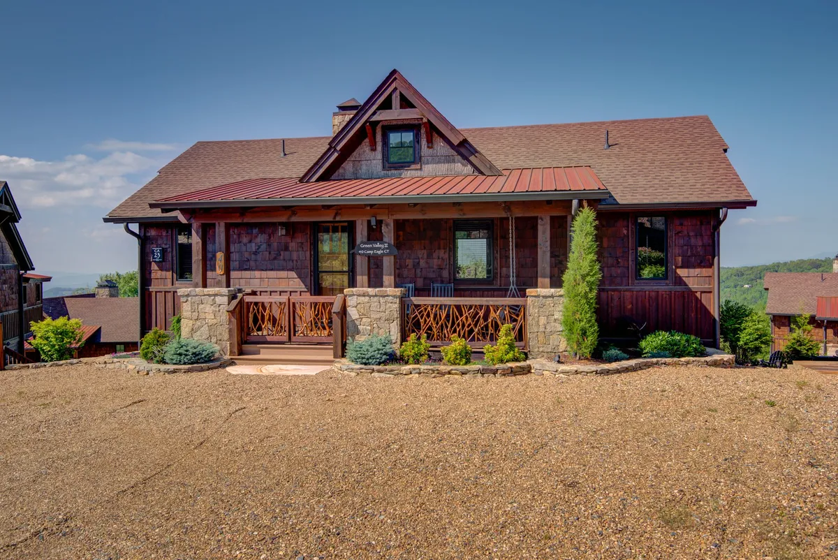 A welcoming front porch framed by stone pillars and wooden shingles, surrounded by lush green landscaping. The area is safe, inviting, and suitable for pets and families to relax and take in the serene mountain air.