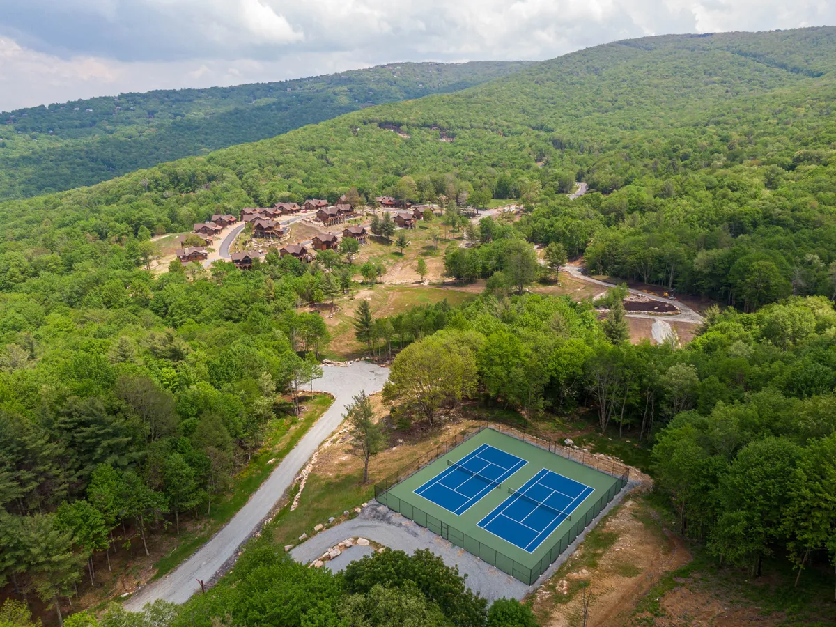 This image showcases a set of tennis courts surrounded by lush greenery, with residential cabins visible in the background. The scene captures the active side of the community, highlighting accessible sports facilities nestled in a natural setting.