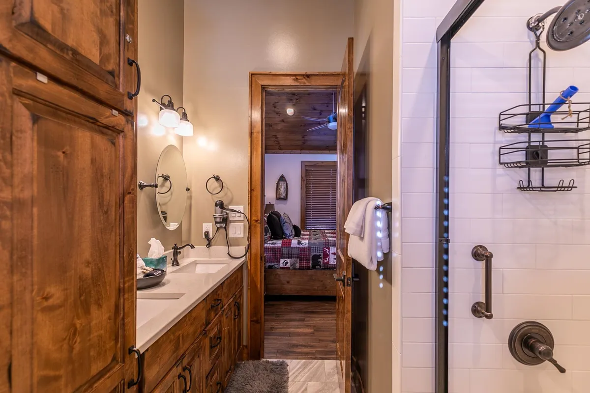 A spacious ensuite bathroom with a double sink vanity, wood cabinets, shower area, and well-lit mirrors. Natural light fills the space, creating a comfortable setting for relaxing morning and evening routines.