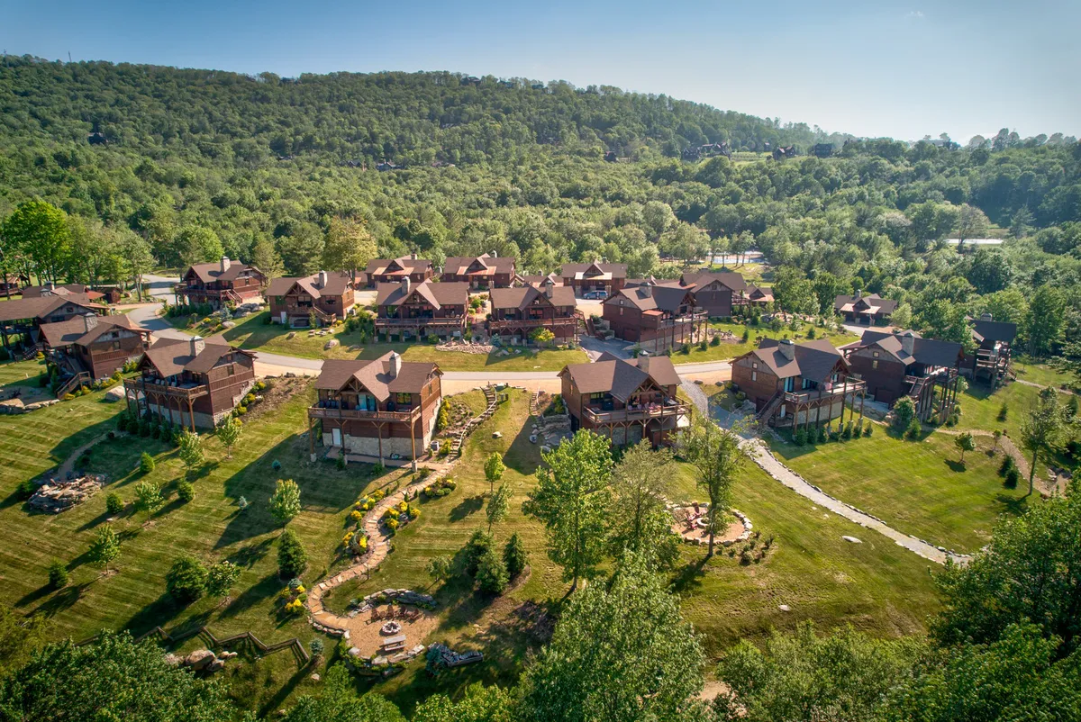 A view of wooden cabins surrounded by landscaped gardens and winding pathways, inviting exploration. The open, green spaces and gentle paths suggest ample opportunity for nature walks with dogs and outdoor adventures.